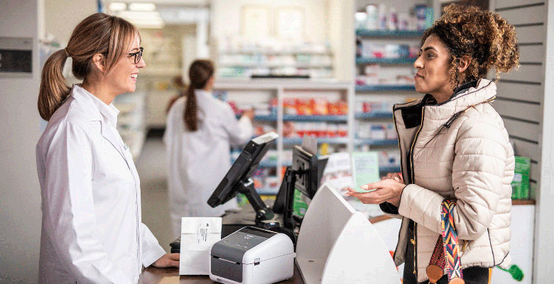 Farmacevtka se pogovarja s stranko za prodajnim pultom z namiznim tiskalnikom Brother TD 