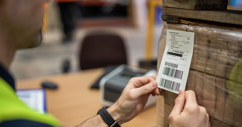 Delavec v tovarni lepi nalepko na paket, natisnjeno s tehnologijo za neposredno termično tiskanje