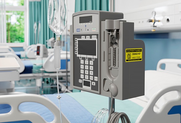Rumena nalepka o vzdrževanju na infuzijski črpalki poleg postelje na bolniškem oddelku 